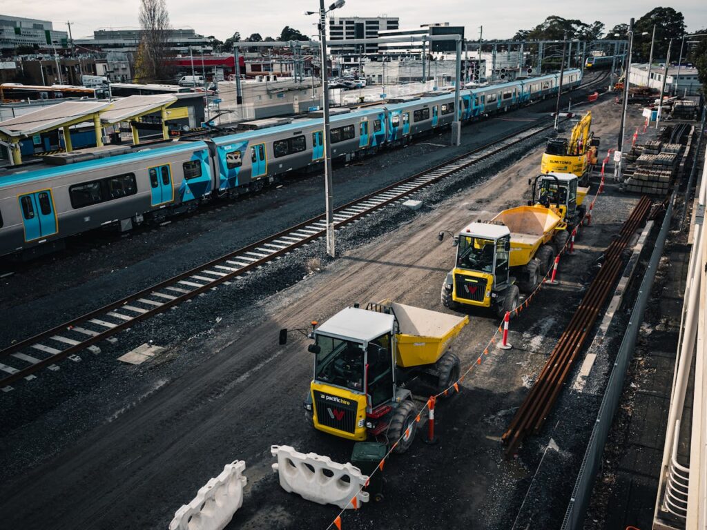 Construction site with yellow machinery and trains at a station.