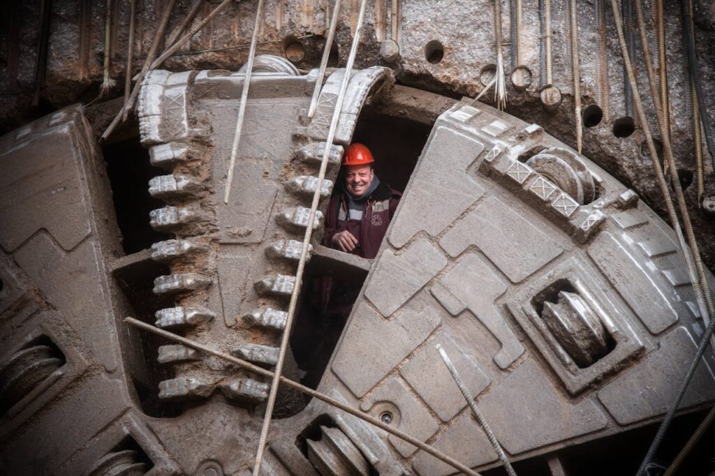 A construction worker smiling from inside a tunnel boring machine.